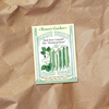 A seed packet featuring an illustration of slender, bright green bush beans growing on compact plants laying on kraft paper.