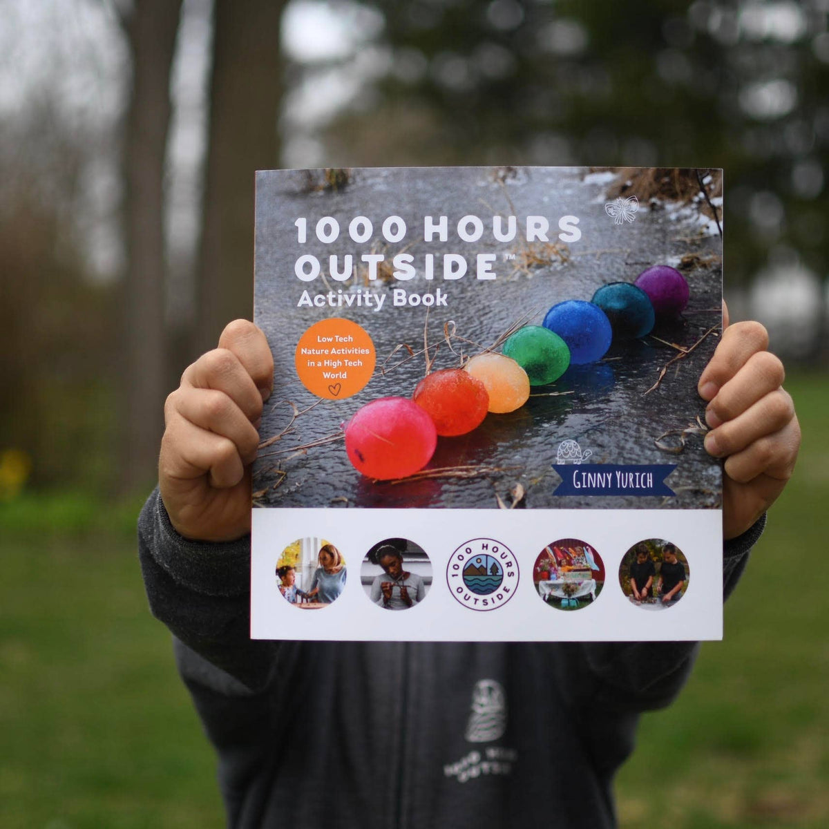 1000 Hours Outside Book being held by a person out of focus from the camera.